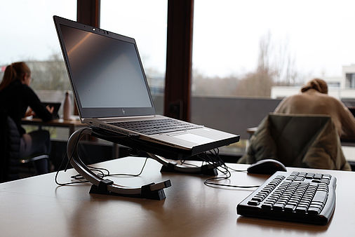 Neigbarer Laptopständer auf Tisch, im Hintergrund Arbeitsplätze