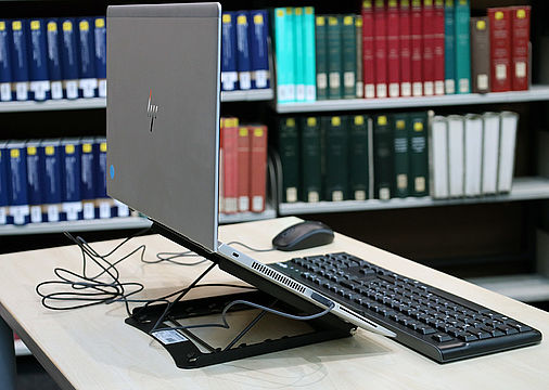 Höhenverstellbarer Laptopständer, im Hintergrund Bücherregale